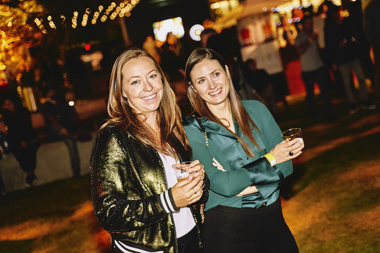 Two women holding cocktails at night.