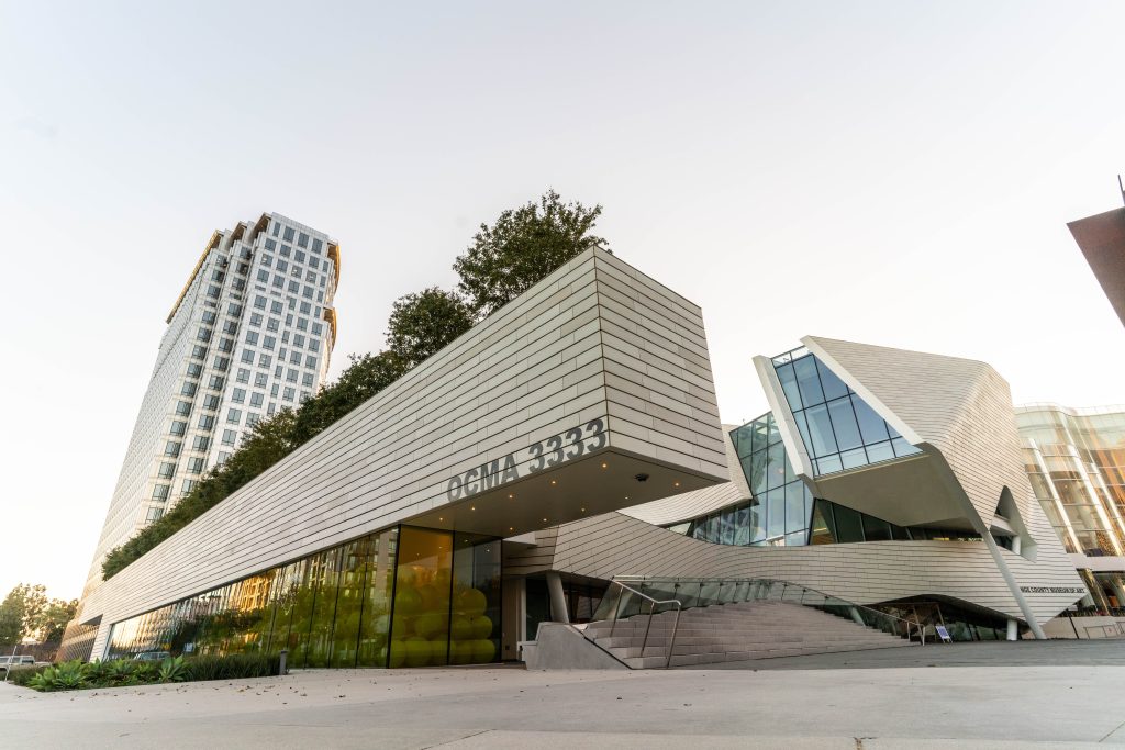 Modern architectural buildings with sharp angles and glass windows, including the entrance to a building labeled “CHILDREN’S,” set against a clear sky with a tall residential tower in the background.