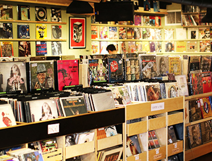 A cozy record store interior in Mesa Verde Costa Mesa, with rows of vinyl albums in bins and colorful covers on the walls. A person browses in the background among shelves filled with records.