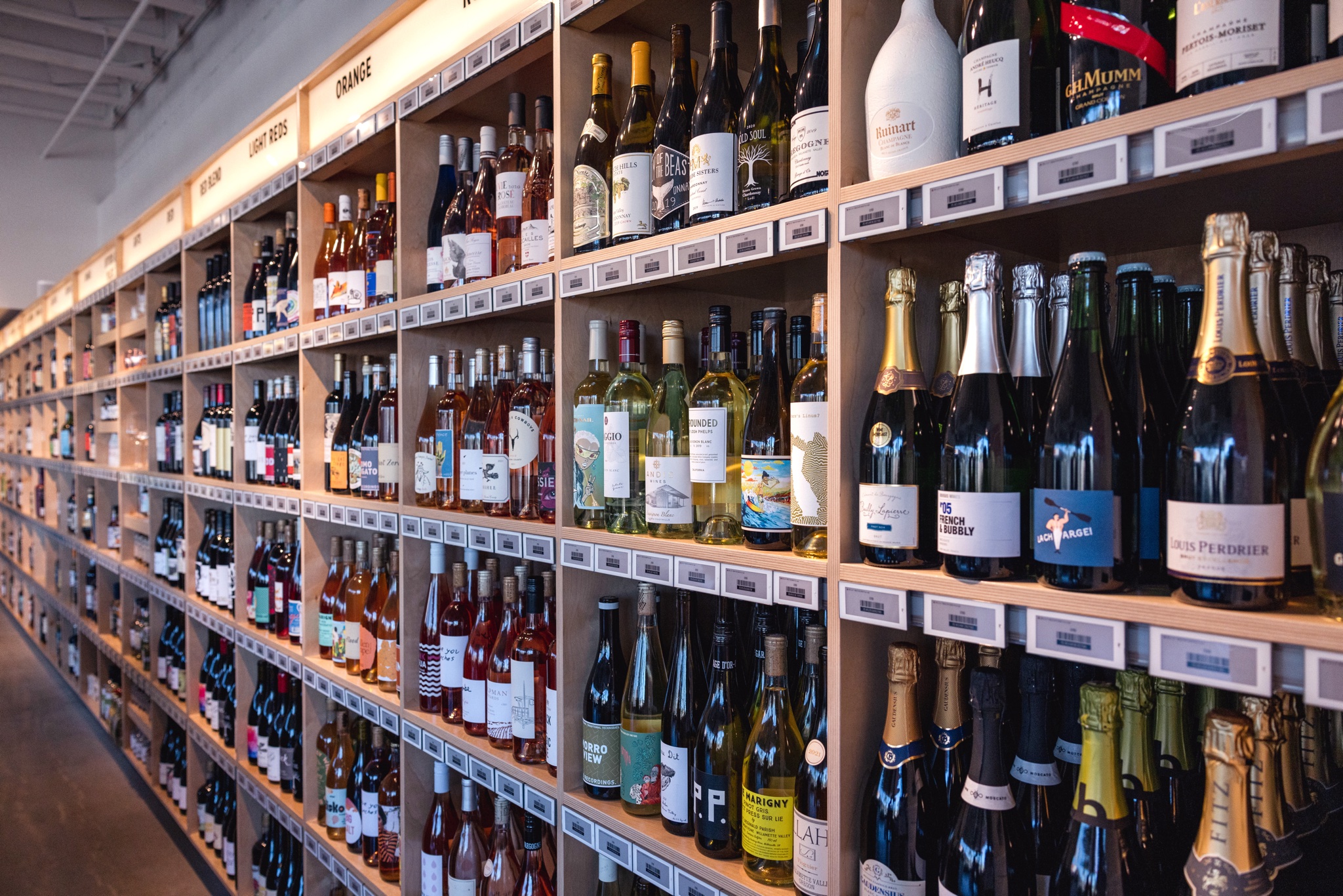 Shelves in a well-lit store display a wide variety of wine and champagne bottles, organized by type and label, stretching down a long aisle—a scene perfect for any Costa Mesa travel blog.
