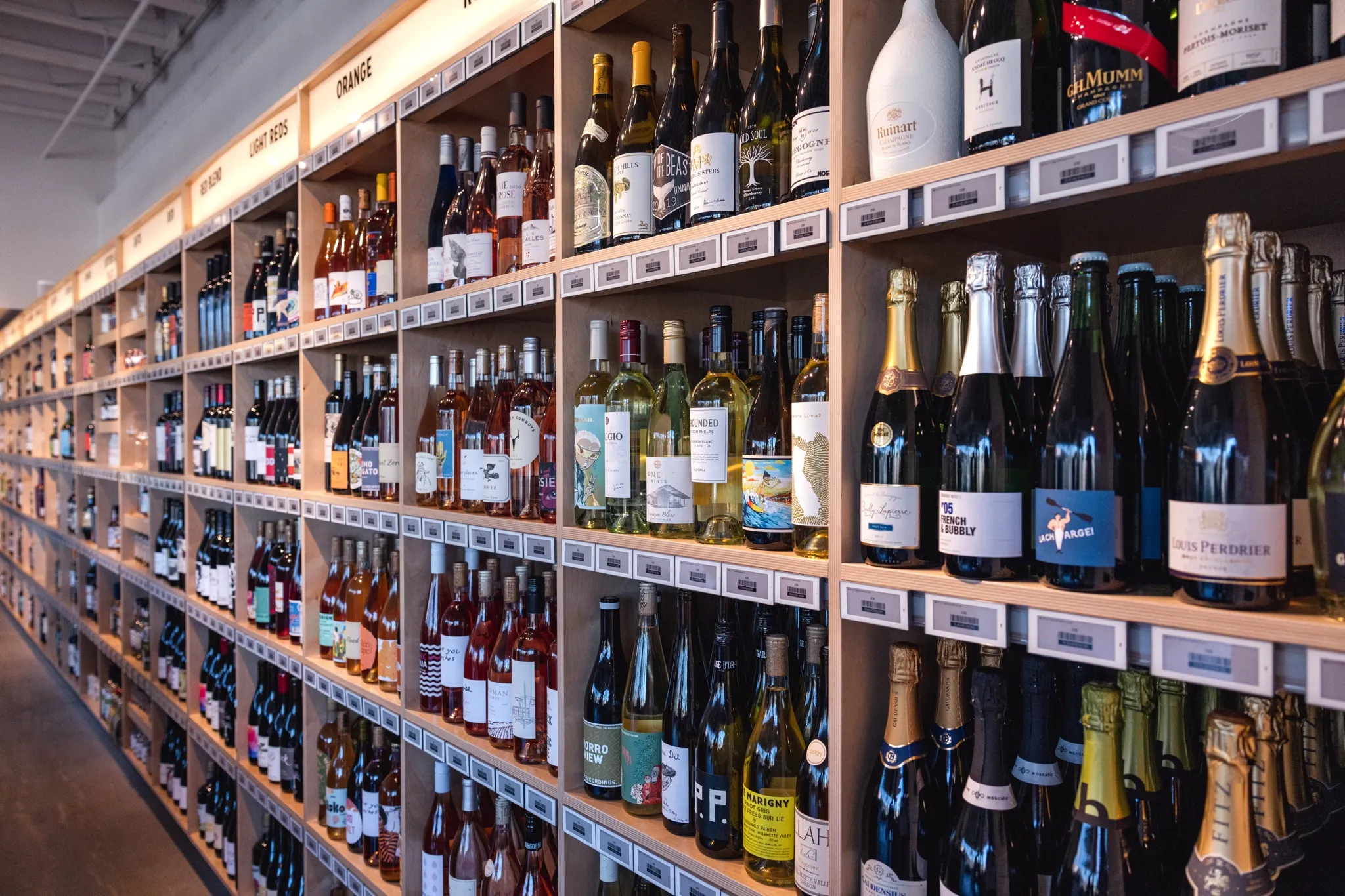 Shelves in a well-lit store display a wide variety of wine and champagne bottles, organized by type and label, stretching down a long aisle—a scene perfect for any Costa Mesa travel blog.