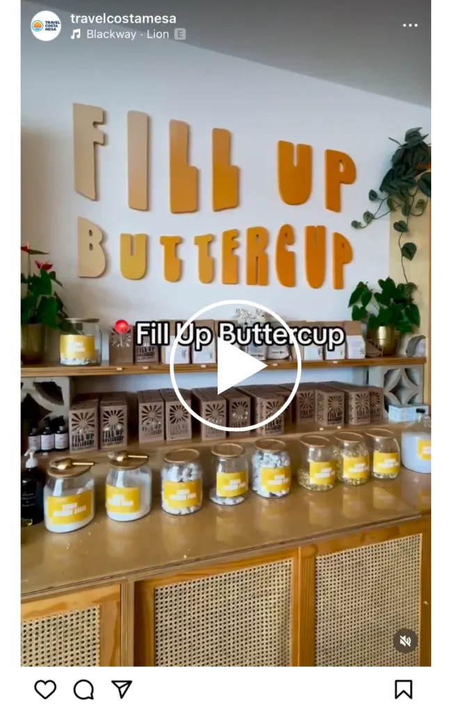 A wooden shelf displays large glass jars filled with various treats, each labeled. Above the shelf, large letters spell out “FILL UP BUTTERCUP” on the wall, with plants and decor completing the cozy setup.