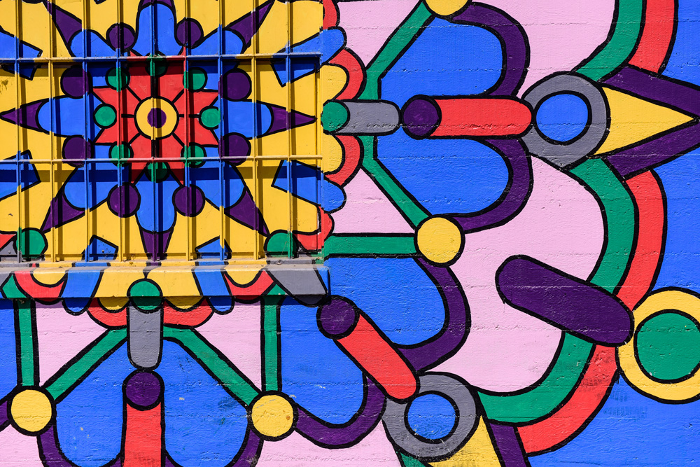 A brightly colored mural with geometric patterns of yellow, blue, pink, red, green, and purple adds vibrant charm to the city—perfect for those wondering where is Costa Mesa.