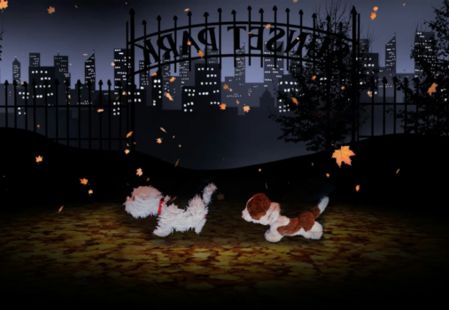 Two small dogs walk on autumn leaves in a dark park at night, with city buildings and a tall iron gate in the background. Orange leaves fall from above, and tree silhouettes frame the scene.