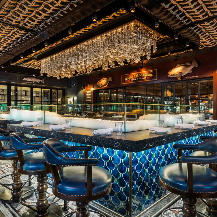 A stylish seafood restaurant bar with blue fish-scale tiles, leather chairs, hanging glass decorations, and a patterned ceiling, giving a luxurious, aquatic-themed ambiance.