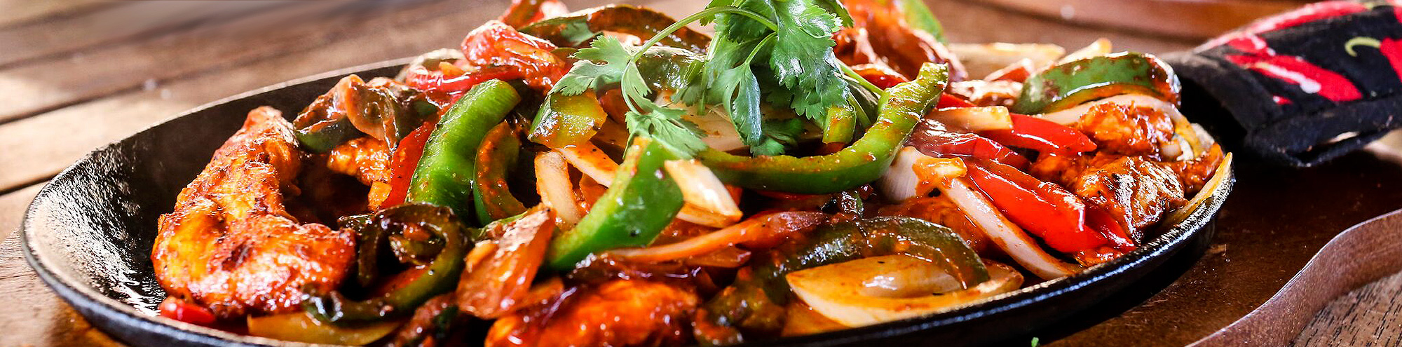 A sizzling skillet filled with grilled chicken strips, bell peppers, onions, and fresh cilantro, served on a wooden table.