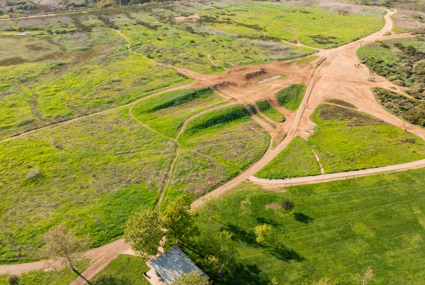 Aerial view of a park with winding dirt paths crossing green fields and patches of grass, trees scattered throughout, and a small structure in the bottom left corner—perfect for a Costa Mesa travel blog feature.