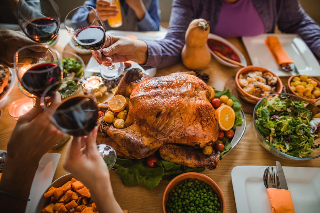 A group of people raise glasses of red wine in a toast over a table set with a roasted turkey, vegetables, salad, and side dishes, creating a festive and celebratory meal atmosphere.