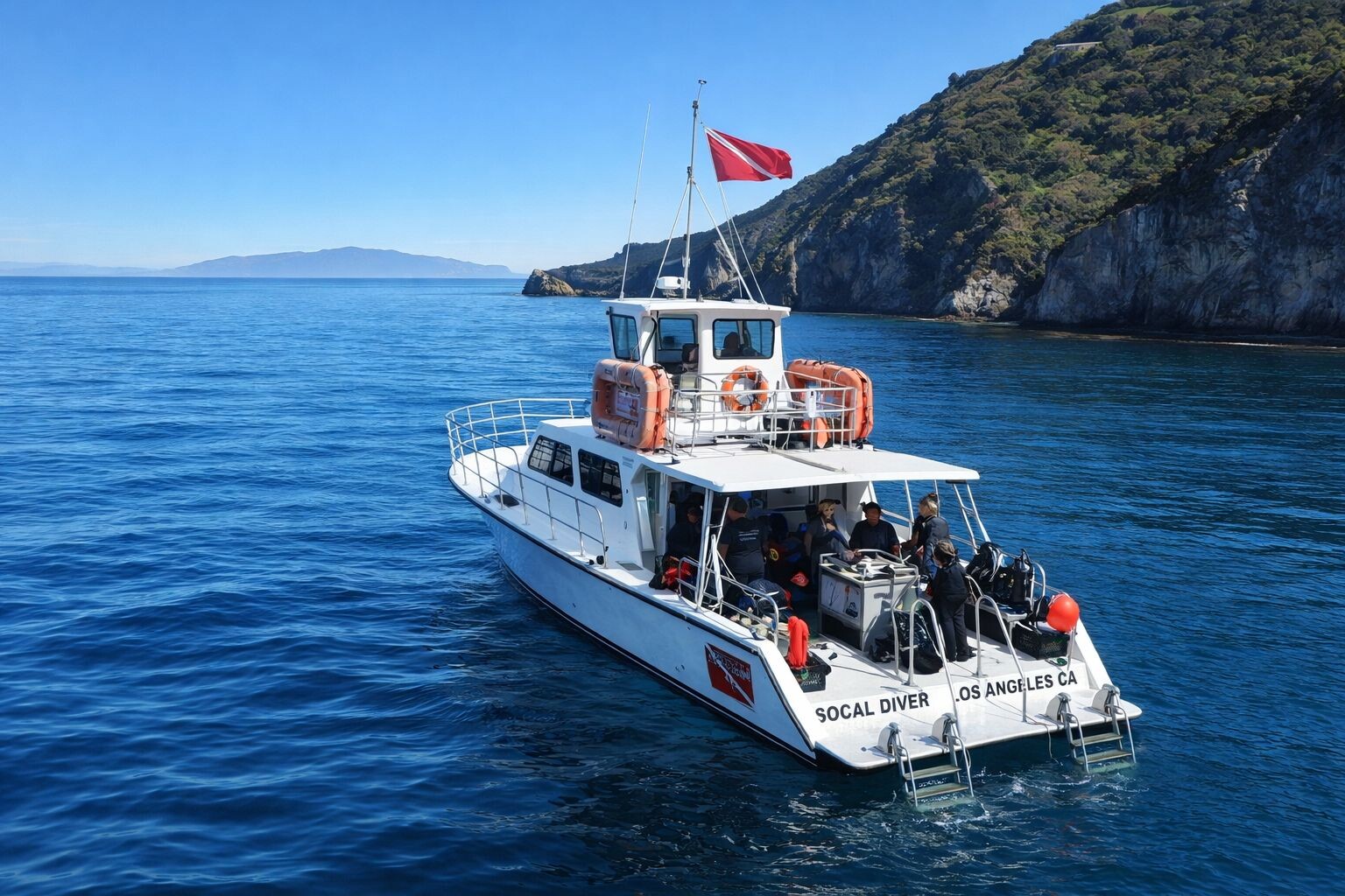 A white dive boat labeled Socal Diver Los Angeles CA floats on clear blue water near a rocky island, not far from Costa Mesa. Several people with diving equipment are on board, enjoying the sunny sky.