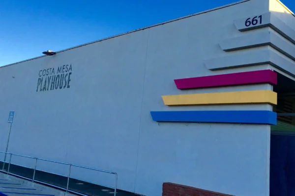 Exterior of the Costa Mesa Playhouse at 661, featuring a white wall with pink, yellow, and blue horizontal accents.