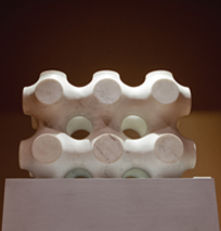A white sculptural object with rounded protrusions and circular holes sits on a pedestal against a dark background, capturing the innovative spirit of the Costa Mesa Art Walk.