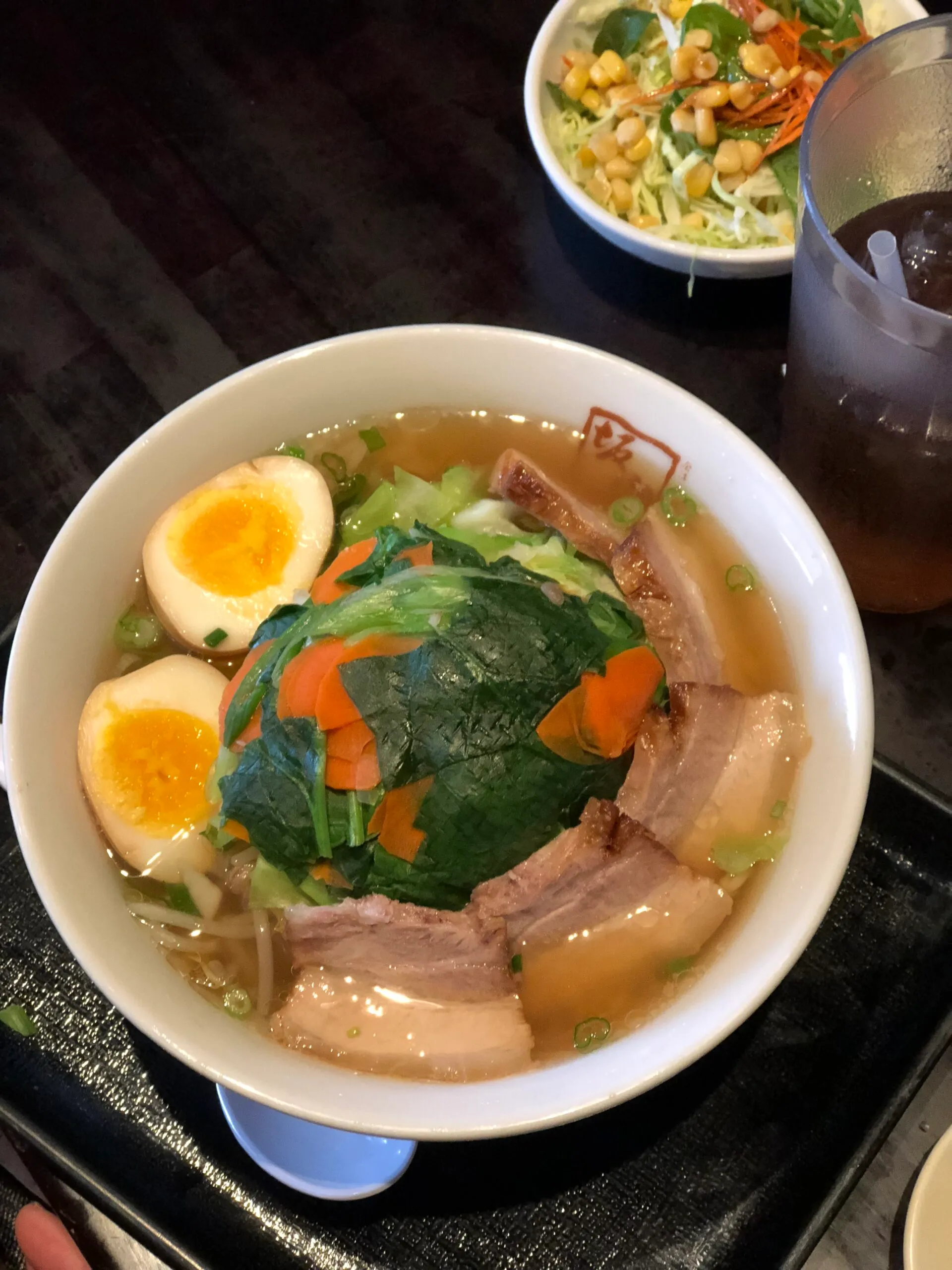 A bowl of Kitakata ramen topped with sliced pork belly, a soft-boiled egg, and greens, served with a side salad and a glass of iced tea at Ban Nai.