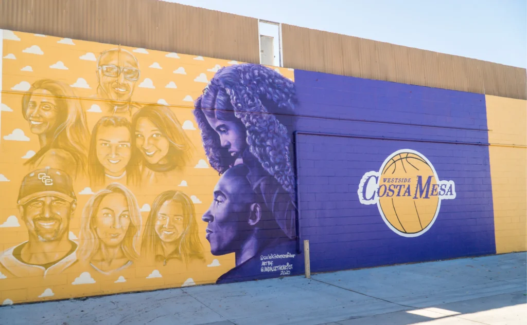 A mural on a wall features yellow and purple tones. On the left, there are realistic portraits of diverse people, while on the right, a large basketball displays Costa Mesa—perfect for any costa mesa travel blog seeking local art.