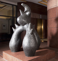 Abstract bronze sculpture with rounded shapes and pointed spikes, resembling a fantastical creature, displayed indoors on a marble pedestal in a modern building lobby along the Costa Mesa Art Walk.