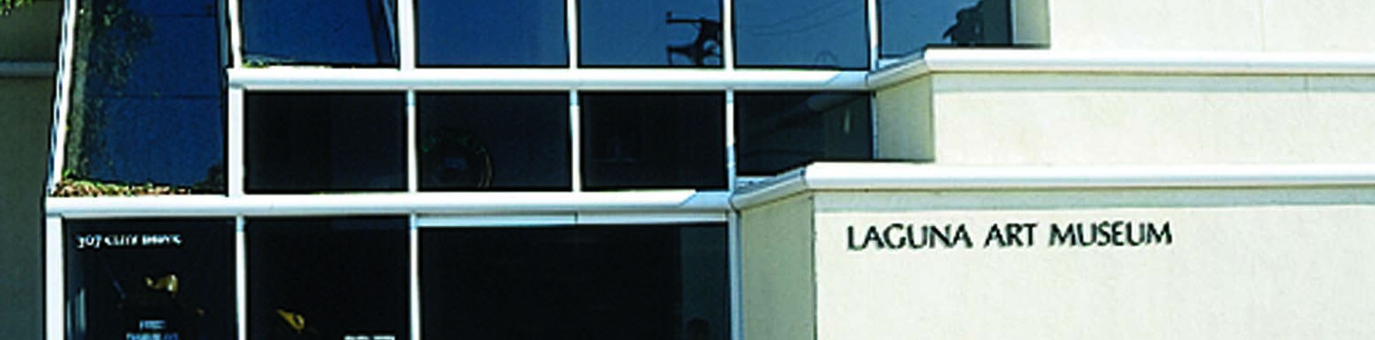 Exterior view of a modern building with large glass windows and a light-colored wall displaying the text Laguna Art Museum.