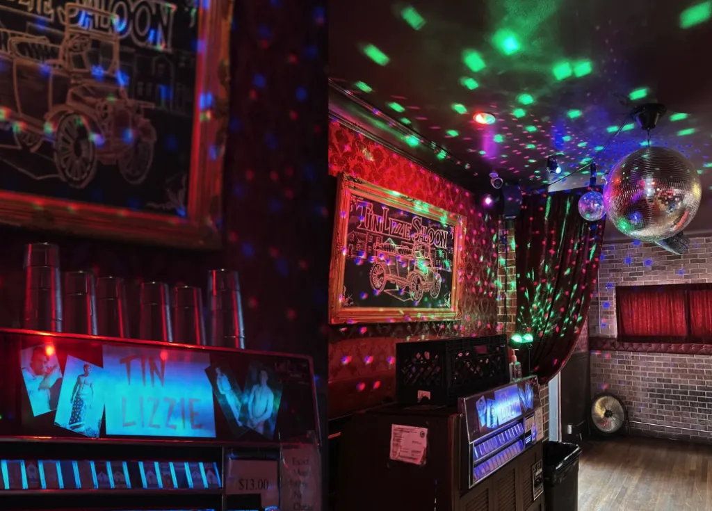 A dimly lit room with colorful disco lights, a mirror ball on the ceiling, red curtains, a chalkboard sign, and a jukebox labeled Tin Lizzie with plastic cups stacked nearby.