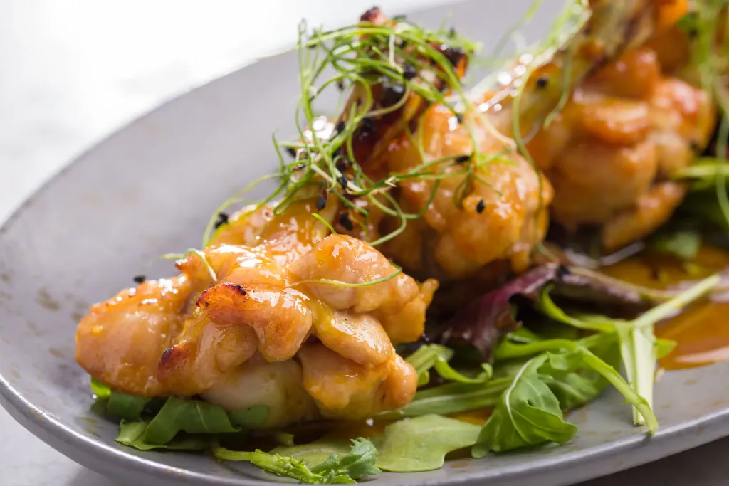 Close-up of glazed chicken drumettes garnished with fresh greens, served on a bed of arugula with a drizzle of sauce on a gray plate.