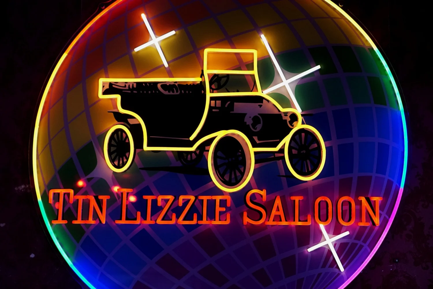Neon sign featuring a vintage car silhouette and the words “Tin Lizzie Saloon,” set against a colorful, glowing disco ball background with bright star highlights.