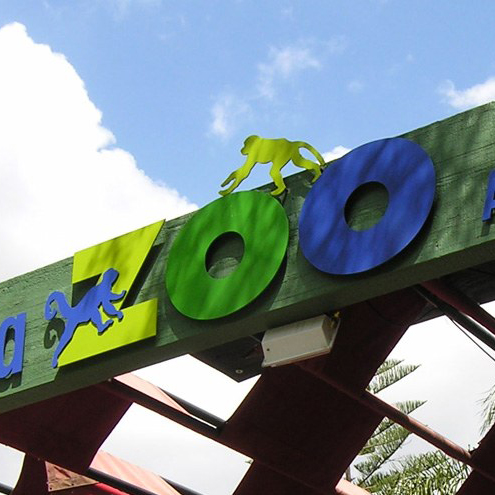 A colorful zoo entrance sign with the word ZOO in large green and blue letters and silhouettes of monkeys on top and on the letter Z, set against a blue sky—perfect for memorable day trips from Costa Mesa.