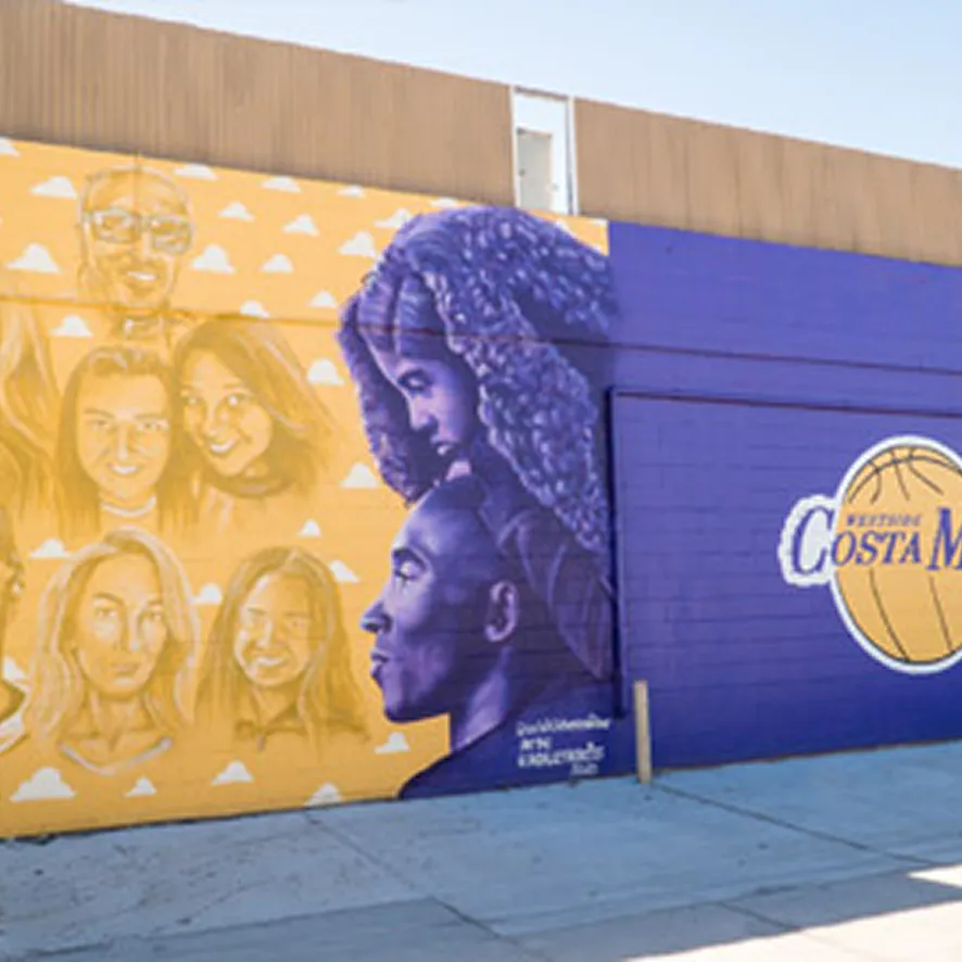 A mural on a building features portraits of several people on a yellow background and two larger figures in profile on purple, welcoming those getting to Costa Mesa from airport. The right side includes a basketball graphic and the words Westside Costa Mesa.