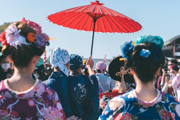 A group of people in colorful traditional Japanese clothing stand outdoors, perfect for those seeking unique cultural experiences among the things to do in Costa Mesa. One person holds a large red parasol; several have flowers and ornaments in their hair.