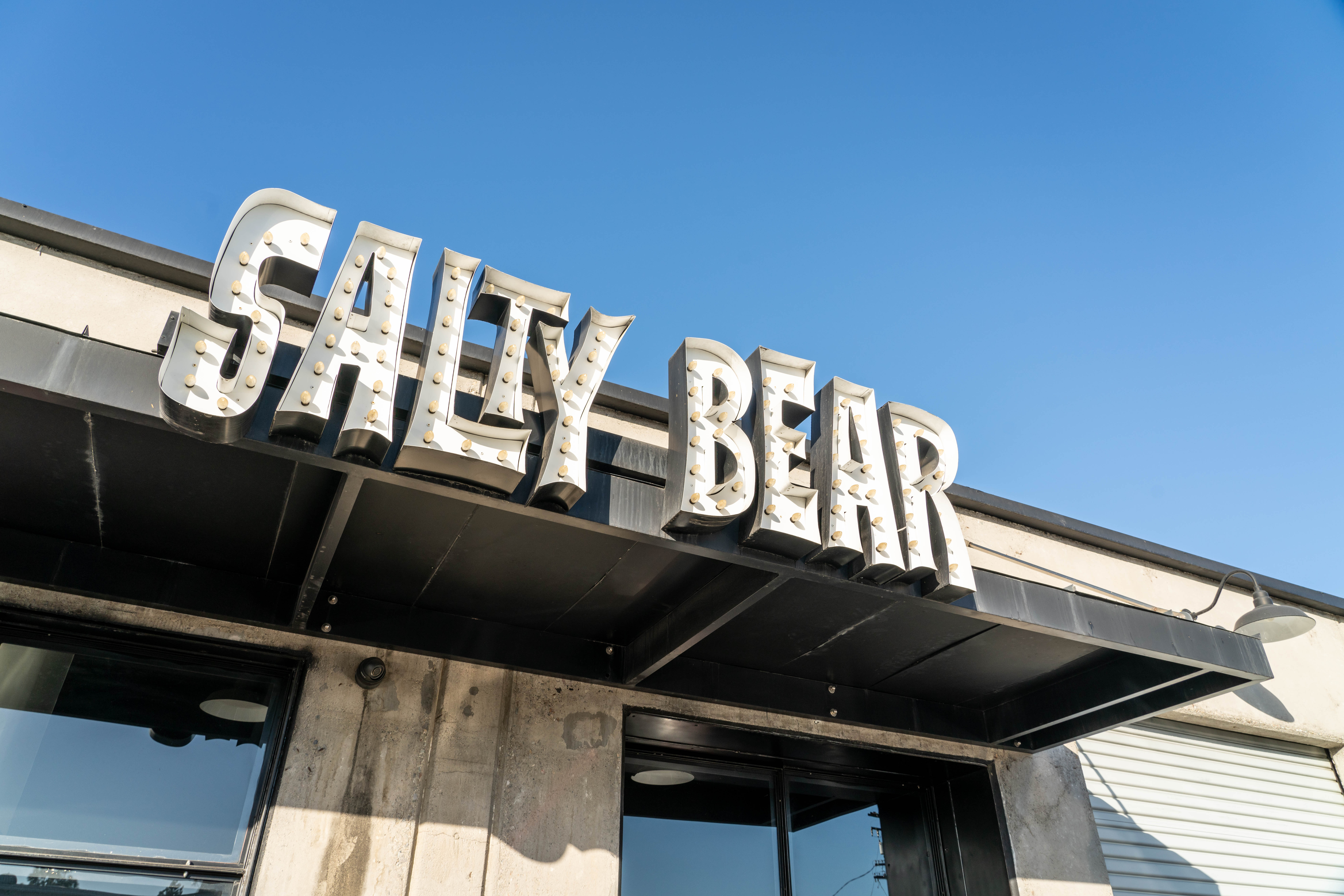A large, retro-style sign reading SALTY BEAR is mounted above the entrance of a modern concrete building beneath a clear blue sky, marking this spot as a standout Costa Mesa brewery.