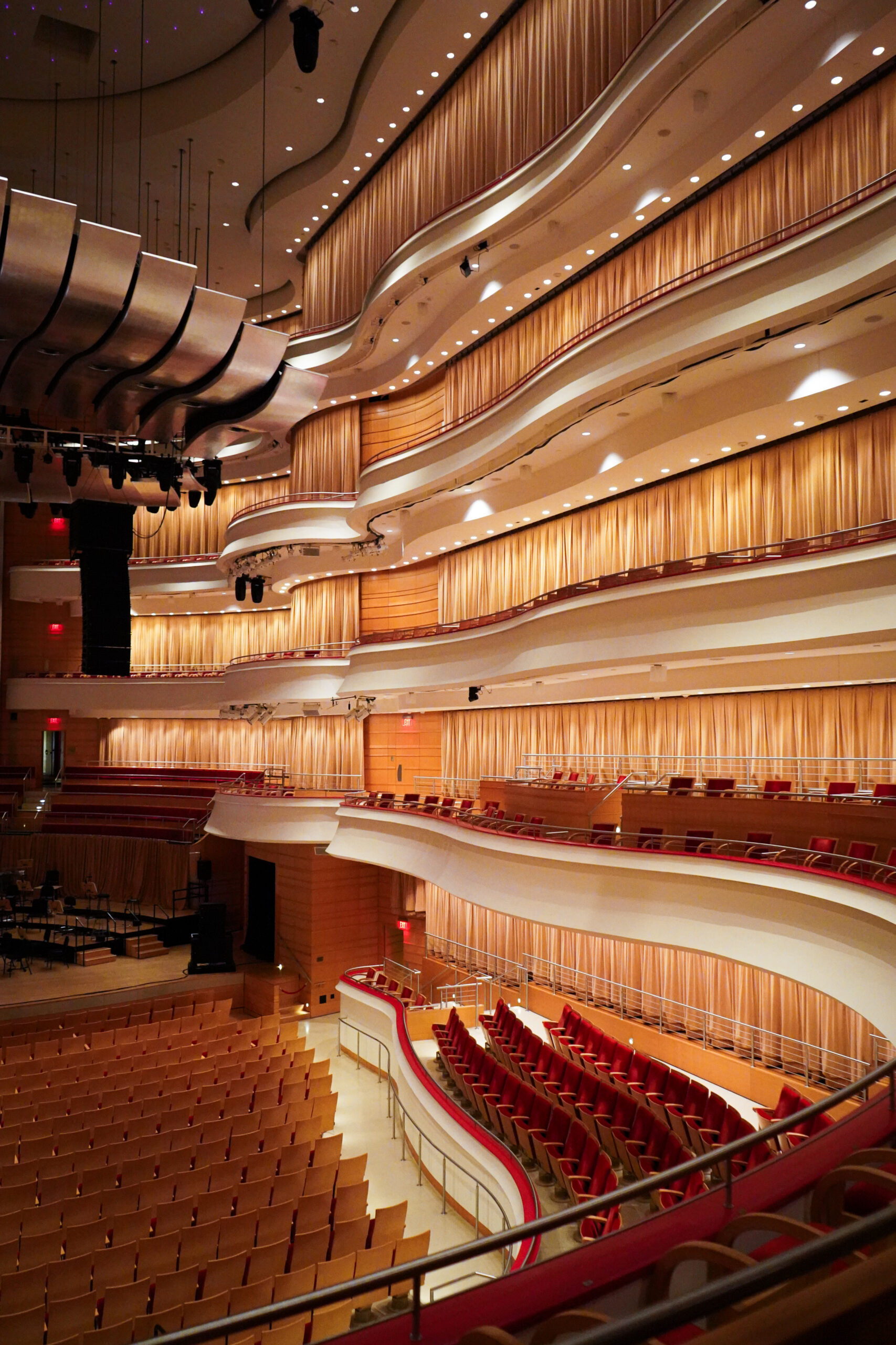 A modern concert hall interior with curved balconies, red seats, and warm lighting. The empty stage and seating area highlight the elegant design, making it a standout among Costa Mesa attractions for architecture enthusiasts.