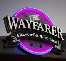 A neon sign reads The Wayfarer: A House of Social Provisions with decorative elements and a glowing purple and blue background.