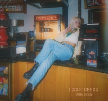 A person with blonde hair, wearing a white top and blue jeans, sits casually on a counter in front of a popcorn machine. The text I DONT NEED U and CASEY CONLEY appears in the lower right corner.