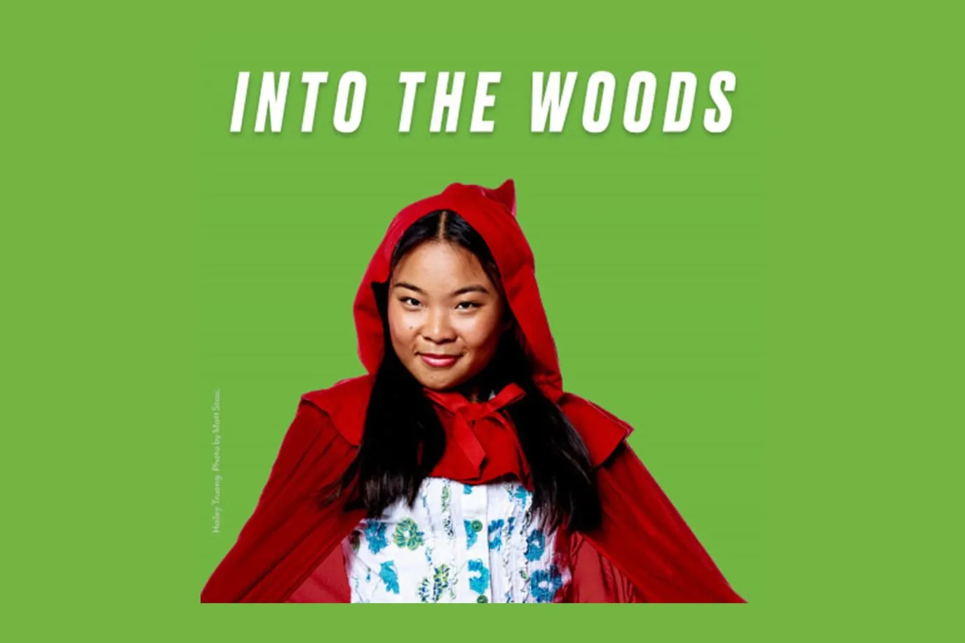 A girl in a red hooded cape smiles against a green background with the words INTO THE WOODS written above her in white bold letters.