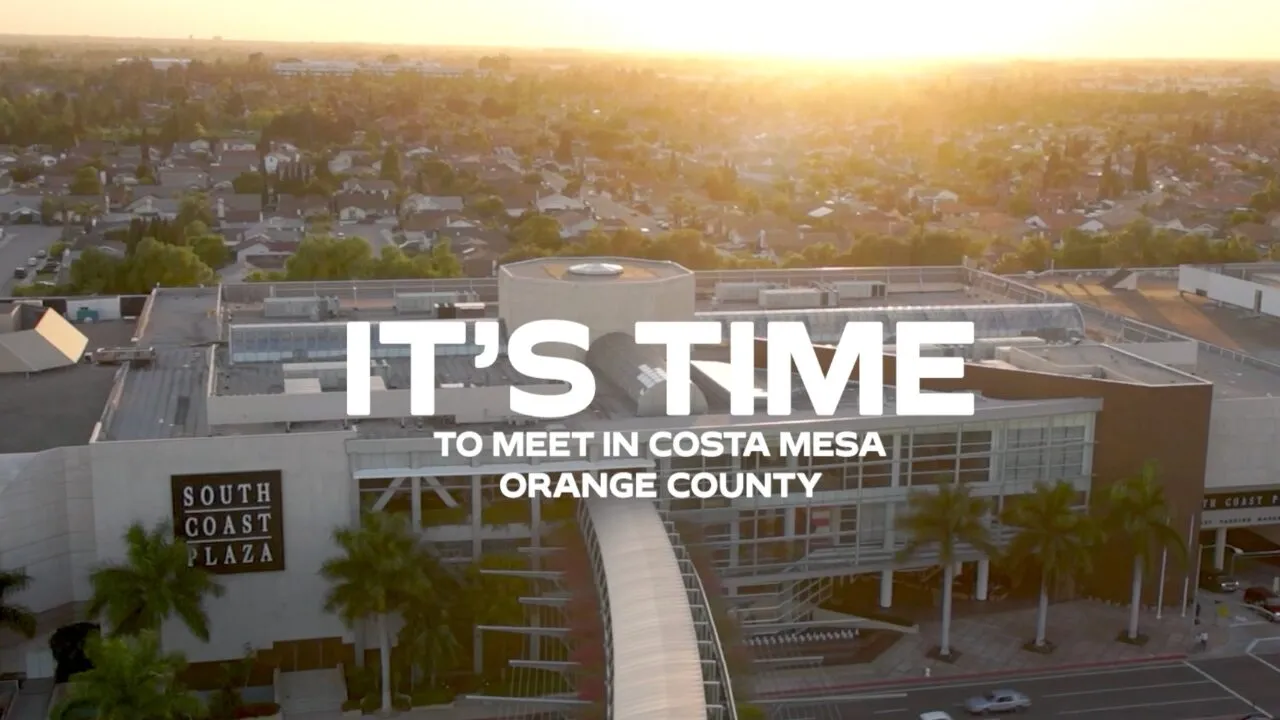 Aerial view of South Coast Plaza with a footbridge and palm trees at sunset. Text reads, ITS TIME TO MEET IN COSTA MESA ORANGE COUNTY—home to premier event venues in Costa Mesa.