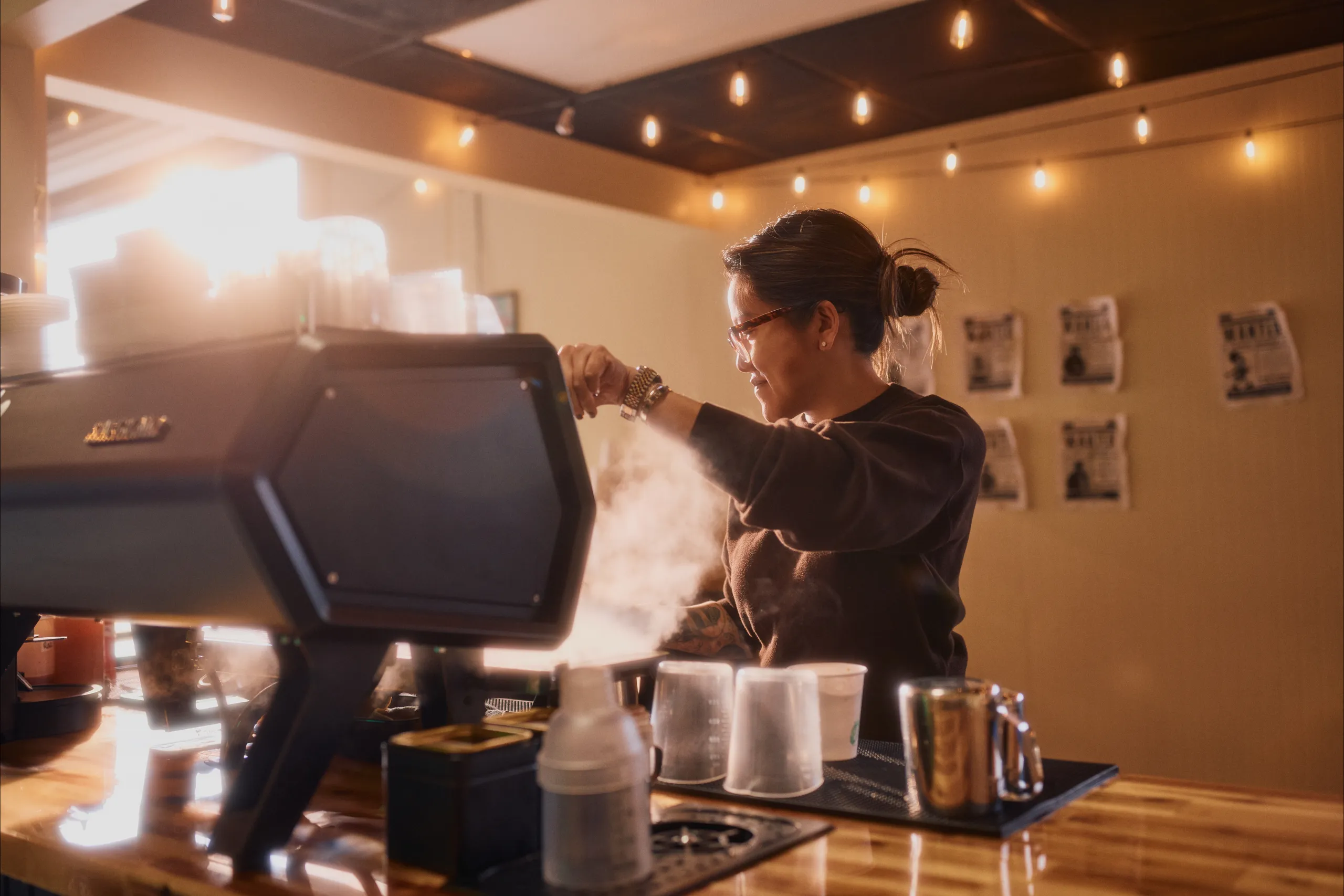 A barista using an espresso machine behind a coffee shop counter in an arts and culture setting.
