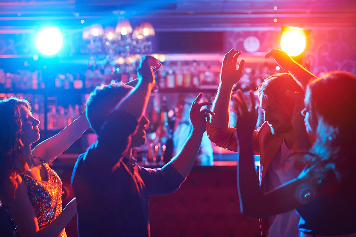 People dancing with their arms raised in a brightly lit nightclub.