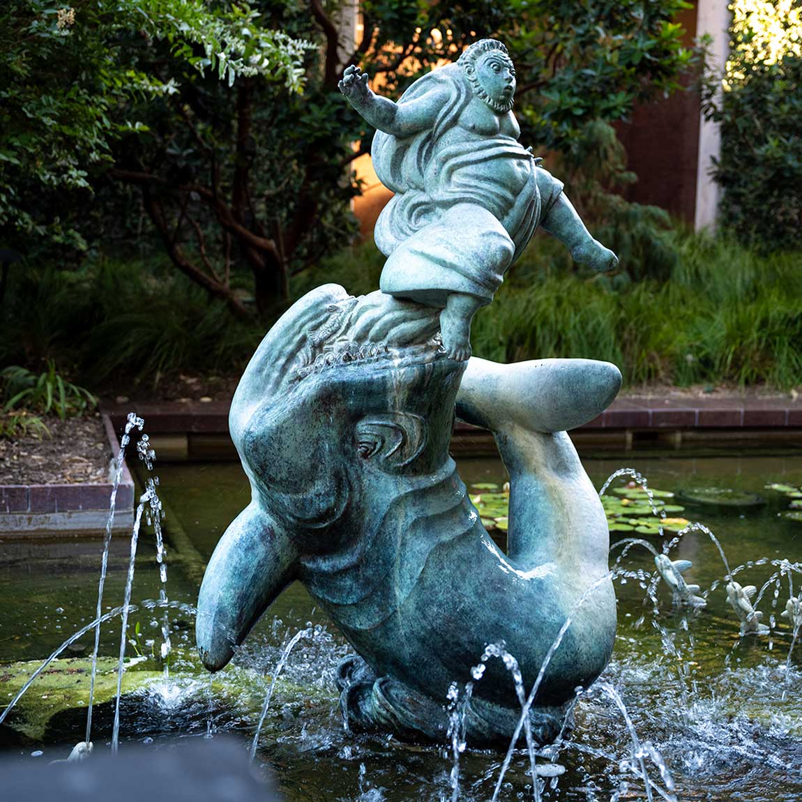 A bronze sculpture of a figure riding on the back of a dolphin in a Costa Mesa Art Walk fountain.